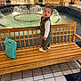 background, bench, camouflage, child, clothing, curious, fountain, indoor, lighting, mall, people, person, plants, shoes, shopping_bag, standing, tile_floor, toddler, water, wooden_bench