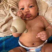 Mazikeen is registered to the contest to win money with this photo: baby, infant, diaper, toy, hand, face, skin, blanket, soft, curious, chubby, indoors, child, cute, expression, lying_down, young, person, closeup, comfort