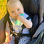 baby, child, stroller, teething_toy, sitting, smiling, outdoor, daylight, clothing, harness, cute, infant, person, face, head, legs, footwear, playful, happy, accessory