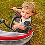 toddler, child, tricycle, outdoor, grass, toy, vehicle, blonde_hair, curious, playing, summer, sunlight, hand, footwear, casual_clothing, expression, seat, handlebar, wheel, person