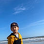 Jules.e a rejoint le concours — aidez-le/la à gagner de superbes lots ! child, boy, beach, sand, ocean, waves, sky, clouds, cap, hoodie, casual_clothing, outdoor, daytime, standing, portrait, young, reflection, nature, water, shore