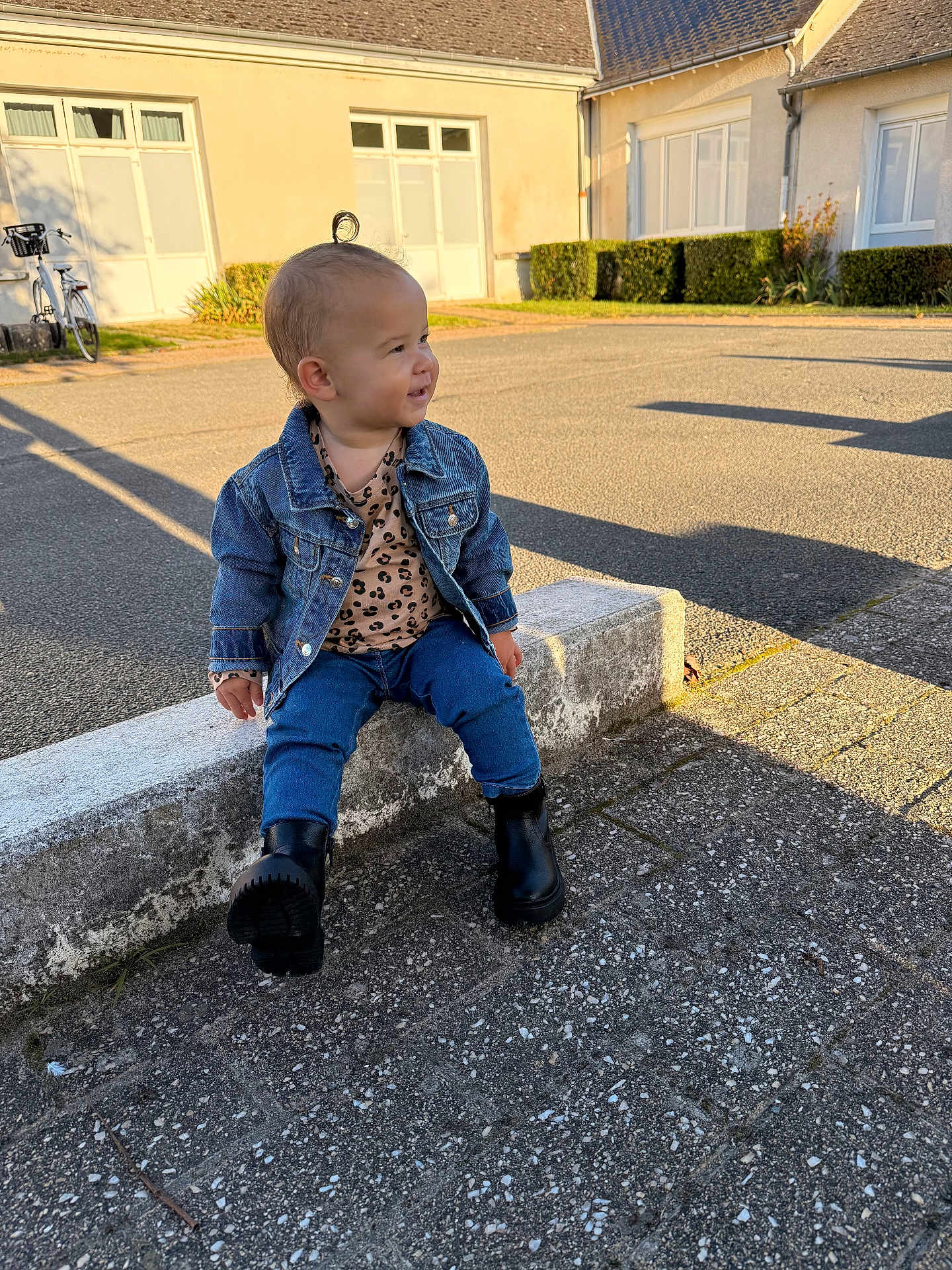 Rose a rejoint le concours — aidez-le/la à gagner de superbes lots ! toddler, child, denim_jacket, leopard_print, jeans, black_boots, outdoor, concrete, pavement, building, shadow, sunlight, curly_hair, topknot, casual_clothing, side_profile, daylight, urban, sitting, young_child