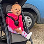 Rose participe au concours pour gagner de l'argent avec cette photo : baby, child, stroller, pink_clothing, floral_leggings, foot, smile, outdoor, gravel, car, wheel, seatbelt, black_stroller, curly_hair, happy, person, sitting, holding_foot, daylight, casual
