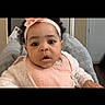 baby, infant, headband, pink, bib, cushion, indoor, person, face, video_call, technology, man, child, curious, seated, portrait, cozy, clothing, expression, communication