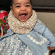 Brazille is registered to the contest to win money with this photo: baby, bib, child, clothing, cute, dress, expression, face, fashion, floral_pattern, hair_accessory, happy, holding, indoor, joy, person, portrait, skin, smiling, young_child