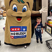 Waylon is registered to the contest to win money with this photo: child, boy, mascot, costume, lollipop, smile, supermarket, grocery_store, shopping_cart, floor, signage, brand_logo, heb, mascot_costume, person, indoor, standing, shoe, happy, eyes