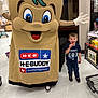 child, boy, mascot, costume, lollipop, smile, supermarket, grocery_store, shopping_cart, floor, signage, brand_logo, heb, mascot_costume, person, indoor, standing, shoe, happy, eyes