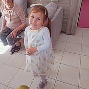 Emma participe au concours pour gagner de l'argent avec cette photo : child, girl, elderly_woman, balloon, white_dress, pink_shoes, hair_clip, smile, indoor, tile_floor, furniture, sofa, cabinet, bag, woman, person, happy, home, casual, portrait