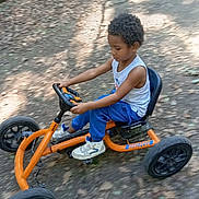 Noé a rejoint le concours — aidez-le/la à gagner de superbes lots ! child, boy, pedal_go_kart, orange, outdoor, path, leaves, sunlight, casual_clothing, white_sneakers, blue_pants, tank_top, curly_hair, motion_blur, nature, play, fun, vehicle, young, concentration