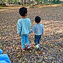 children, walking, forest, autumn, leaves, nature, outdoor, path, holding_hands, curly_hair, casual_clothing, trees, bench, daylight, siblings, playful, young, toddler, jeans, sneakers