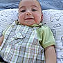 baby, child, smile, face, clothing, overalls, pillow, pattern, elephant, cloud, green_shirt, infant, cute, young_child, happy, closeup, portrait, lying_down, outdoor, soft_light
