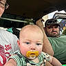 baby, pacifier, man, woman, glasses, cap, vehicle, window, mural, child, portrait, casual, clothing, indoor, person, seat, green_shirt, striped_shirt, blue_eyes, facial_expression