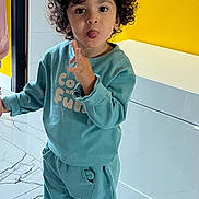 Noha a rejoint le concours — aidez-le/la à gagner de superbes lots ! child, toddler, curly_hair, playful, indoor, yellow_wall, white_cabinet, teal_outfit, sneakers, tongue_out, marvel_shoes, smiling, happy, person, floor, home, casual_clothing, cute, fun, standing