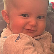 Ridley joined the competition — help win amazing prizes! baby, infant, child, face, smile, eyes, cheek, ear, bald_head, onesie, dinosaur_print, blanket, bedding, couch, indoor, portrait, close_up, happy, skin, gaze