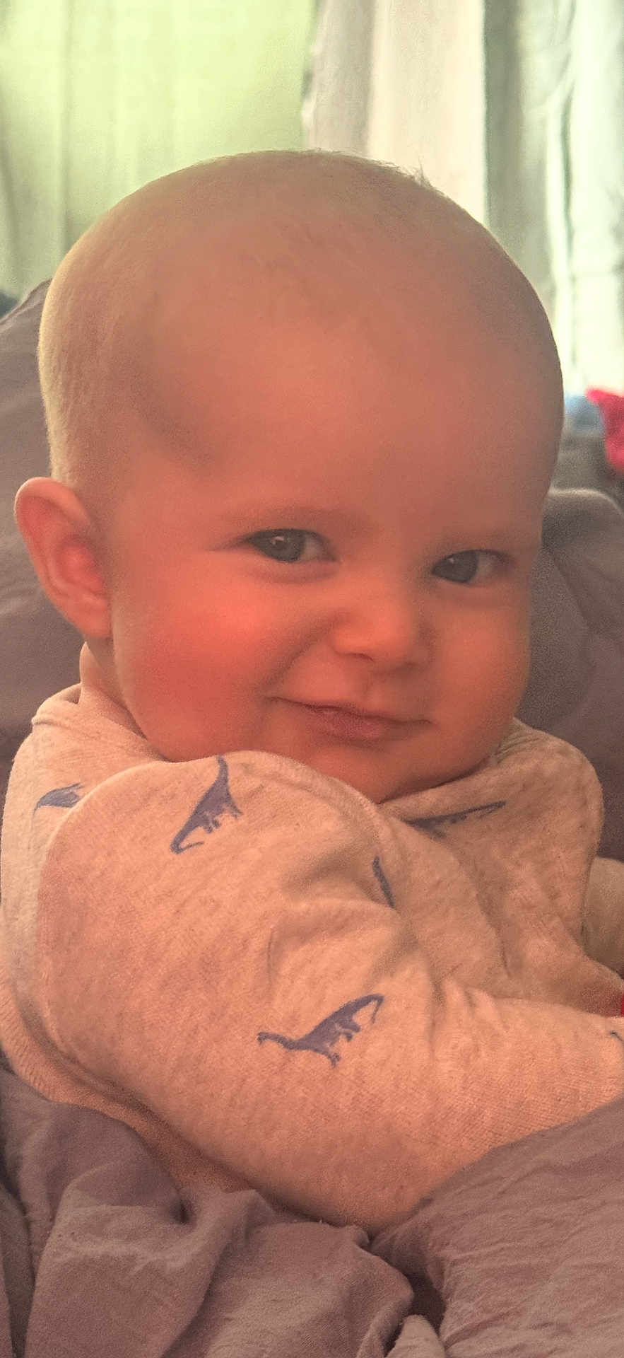 Ridley joined the competition — help win amazing prizes! baby, infant, child, face, smile, eyes, cheek, ear, bald_head, onesie, dinosaur_print, blanket, bedding, couch, indoor, portrait, close_up, happy, skin, gaze