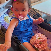 Asiye is registered to the contest to win money with this photo: toddler, child, pacifier, blue_outfit, pink_hair_clip, stroller, flower, orange_shoes, leather_cushion, indoor, cute, baby, portrait, sitting, table, hand, face, head, furniture, soft_lighting