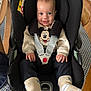 baby, car_seat, child, mickey_mouse, sweater, socks, smile, face, hands, clothing, seatbelt, patterned_tablecloth, wooden_chair, indoor, person, infant, happy, cute, comfort, portrait