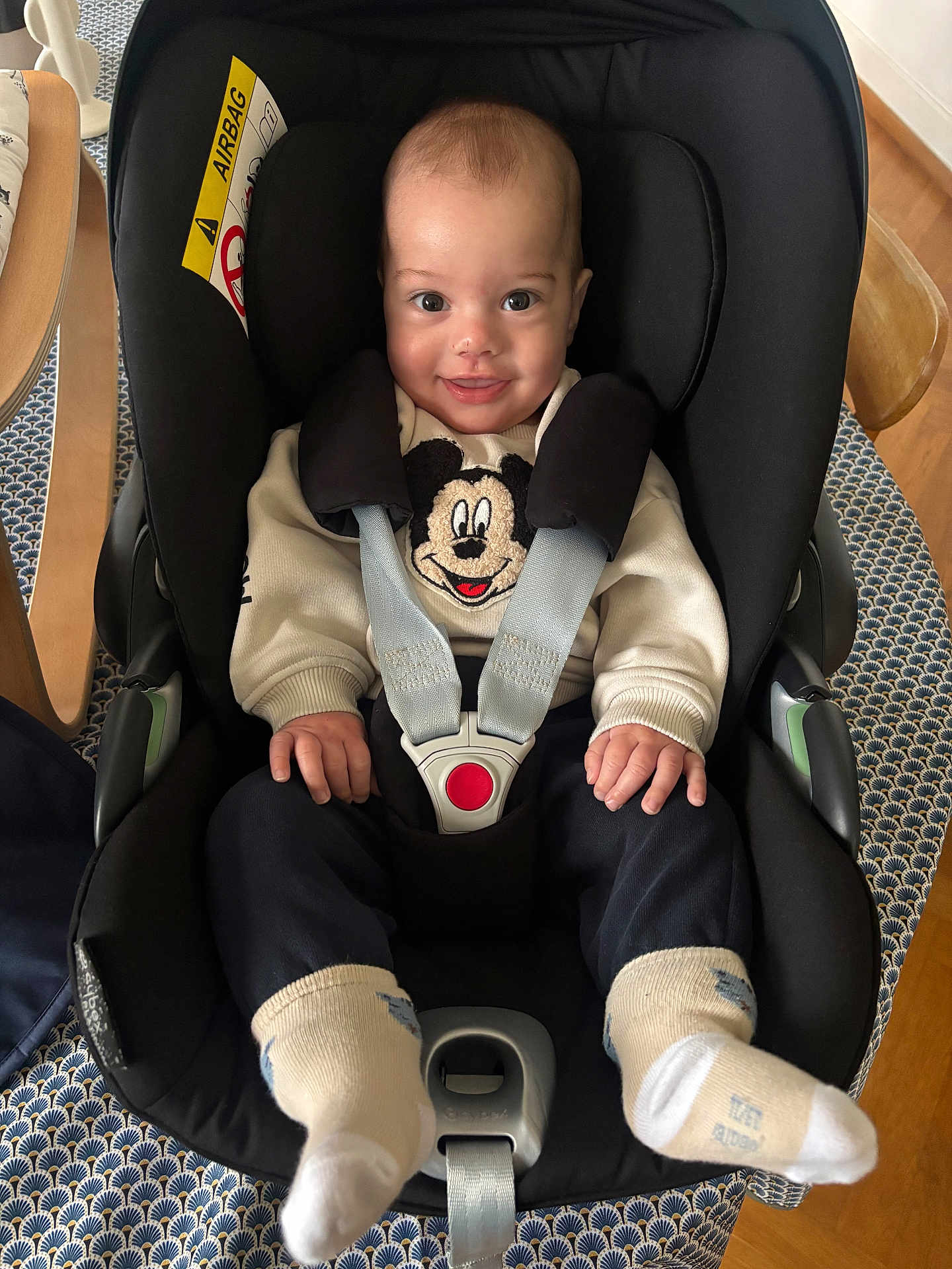 Martin a rejoint le concours — aidez-le/la à gagner de superbes lots ! baby, car_seat, child, mickey_mouse, sweater, socks, smile, face, hands, clothing, seatbelt, patterned_tablecloth, wooden_chair, indoor, person, infant, happy, cute, comfort, portrait