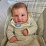 baby, infant, pacifier, blanket, striped_clothing, bib, cushion, baby_chair, face, person, child, indoors, seated, cute, young, skin, hand, expression, comfort, fabric