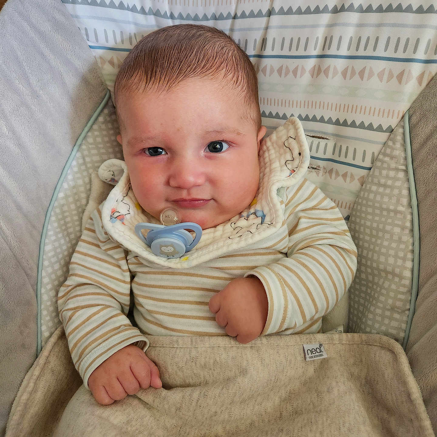Ezekiel joined the competition — help win amazing prizes! baby, infant, pacifier, blanket, striped_clothing, bib, cushion, baby_chair, face, person, child, indoors, seated, cute, young, skin, hand, expression, comfort, fabric