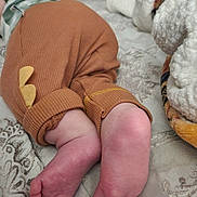 Ezekiel is registered to the contest to win money with this photo: baby, feet, legs, brown_pants, yellow_patch, bedspread, blanket, soft_texture, cozy, infant, sleeping, close_up, skin, toes, fabric, comfort, home, indoor, child, resting