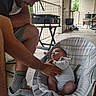 Ezekiel is registered to the contest to win money with this photo: baby, man, baby_rocker, cap, porch, cushion, striped_clothing, footwear, sneakers, socks, facial_hair, hand, floor, door, railing, plant, table, chair, indoor, interaction