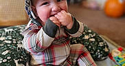 Ezekiel joined the competition — help win amazing prizes! baby, blurred_background, child, colorful, cozy, cushion, finger_biting, happy, hat, indoors, infant, orange_ball, patterned_fabric, plaid_clothing, play_mat, playroom, portrait, sitting, smiling, toys