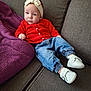 baby, blue_jeans, bow, casual, child, clothing, couch, cozy, footwear, gray_couch, headband, indoors, infant, person, portrait, purple_blanket, red_cardigan, relaxing, seated, white_shoes