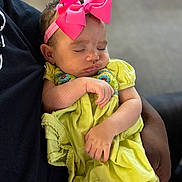Milani joined the competition — help win amazing prizes! baby, sleeping, pink_bow, yellow_dress, infant, child, arm, hand, adult, holding, closeup, portrait, soft_light, indoor, cute, peaceful, tender, clothing, headband, person