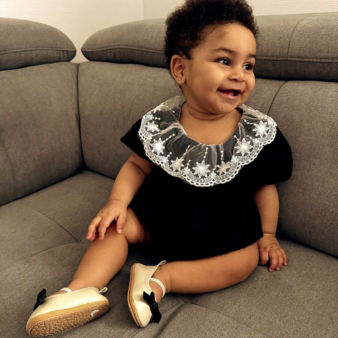 Bassa participe au concours pour gagner de l'argent avec cette photo : adorable, baby, black_outfit, child, couch, cozy, curly_hair, cute, gray_couch, happy, indoor, infant, lace_collar, person, portrait, shoes, sitting, small_feet, smile, young_child