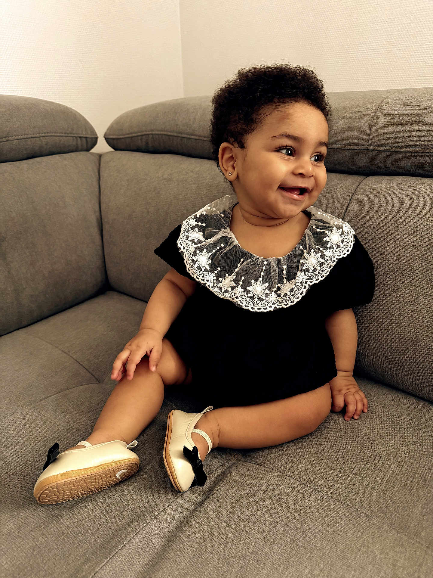 Bassa participe au concours pour gagner de l'argent avec cette photo : baby, child, smile, curly_hair, black_outfit, lace_collar, shoes, couch, gray_couch, sitting, happy, indoor, cute, portrait, young_child, small_feet, adorable, person, infant, cozy
