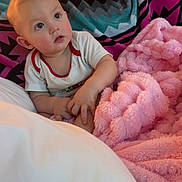 Avery joined the competition — help win amazing prizes! baby, child, blanket, cozy, indoors, soft_texture, pink_blanket, patterned_blanket, white_shirt, curious_expression, face, hands, seated, couch, home, comfort, portrait, young_child, infant, warm_lighting
