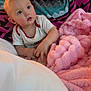 baby, child, blanket, cozy, indoors, soft_texture, pink_blanket, patterned_blanket, white_shirt, curious_expression, face, hands, seated, couch, home, comfort, portrait, young_child, infant, warm_lighting