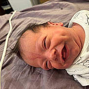Noah is registered to the contest to win money with this photo: baby, newborn, smiling, lying_down, onesie, white_clothing, bed_sheet, purple, infant, face, cute, happy, indoors, soft, skin, hair, portrait, child, sleepwear, resting
