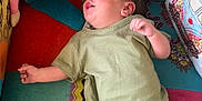 Noah is registered to the contest to win money with this photo: baby, infant, plush_doll, colorful_couch, patterned_cushion, green_pajamas, soft_fabric, toy, child, indoor, pillow, decorative, cute, lying_down, small_feet, cozy, childhood, playful, textile, comfort
