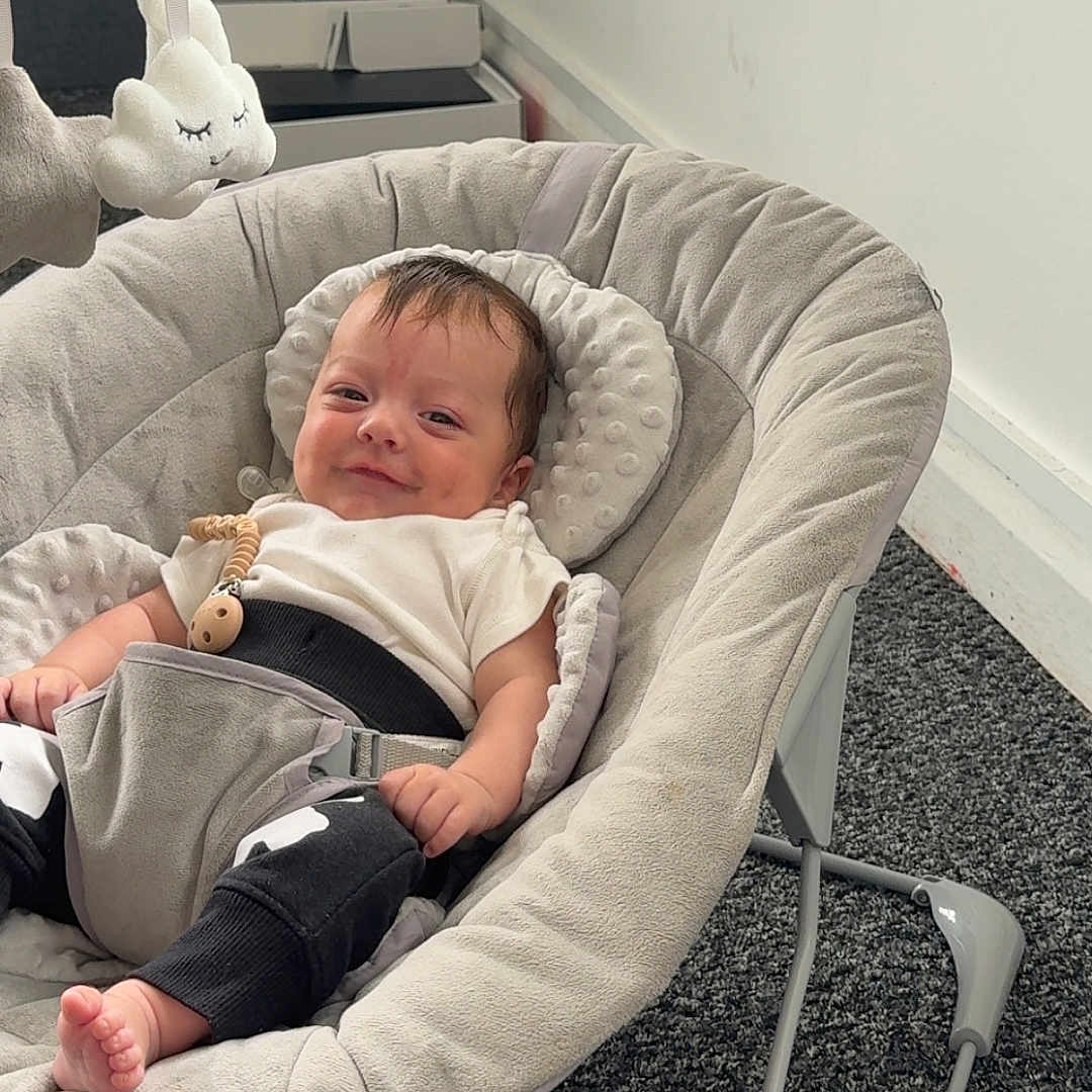 Noah is registered to the contest to win money with this photo: baby, baby_rocker, carpet, child, clothing, comfort, cute, gray, head, indoor, infant, person, plush_toy, relaxing, seat, smile, smiling, soft, toy, young