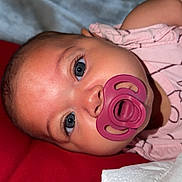 Gaia is registered to the contest to win money with this photo: baby, pacifier, face, infant, lying_down, red_blanket, pink_clothing, closeup, blue_eyes, skin, head, newborn, indoors, soft_texture, blanket, child, portrait, cute, sleepwear, human