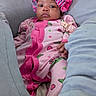baby, infant, pink_bonnet, pink_onesie, hearts_pattern, frog_pattern, cushions, legs, gray_pants, indoor, portrait, cute, cozy, child, relaxed, seated, clothing, soft_fabric, home, newborn