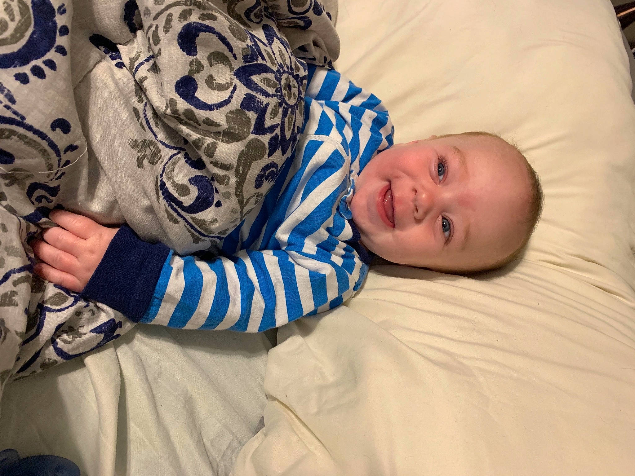 Creed is registered to the contest to win money with this photo: baby, baby_toddler_clothing, bedtime, child, comfort, couch, electric_blue, eye, happy, head, human_body, linens, mouth, nose, pattern, person, room, sitting, skin, sleeve