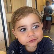 Jaxson is registered to the contest to win money with this photo: child, toddler, face, portrait, indoor, table, clothing, shirt, blue, hair, eyes, person, smile, cute, young, sitting, background, blur, adult, furniture