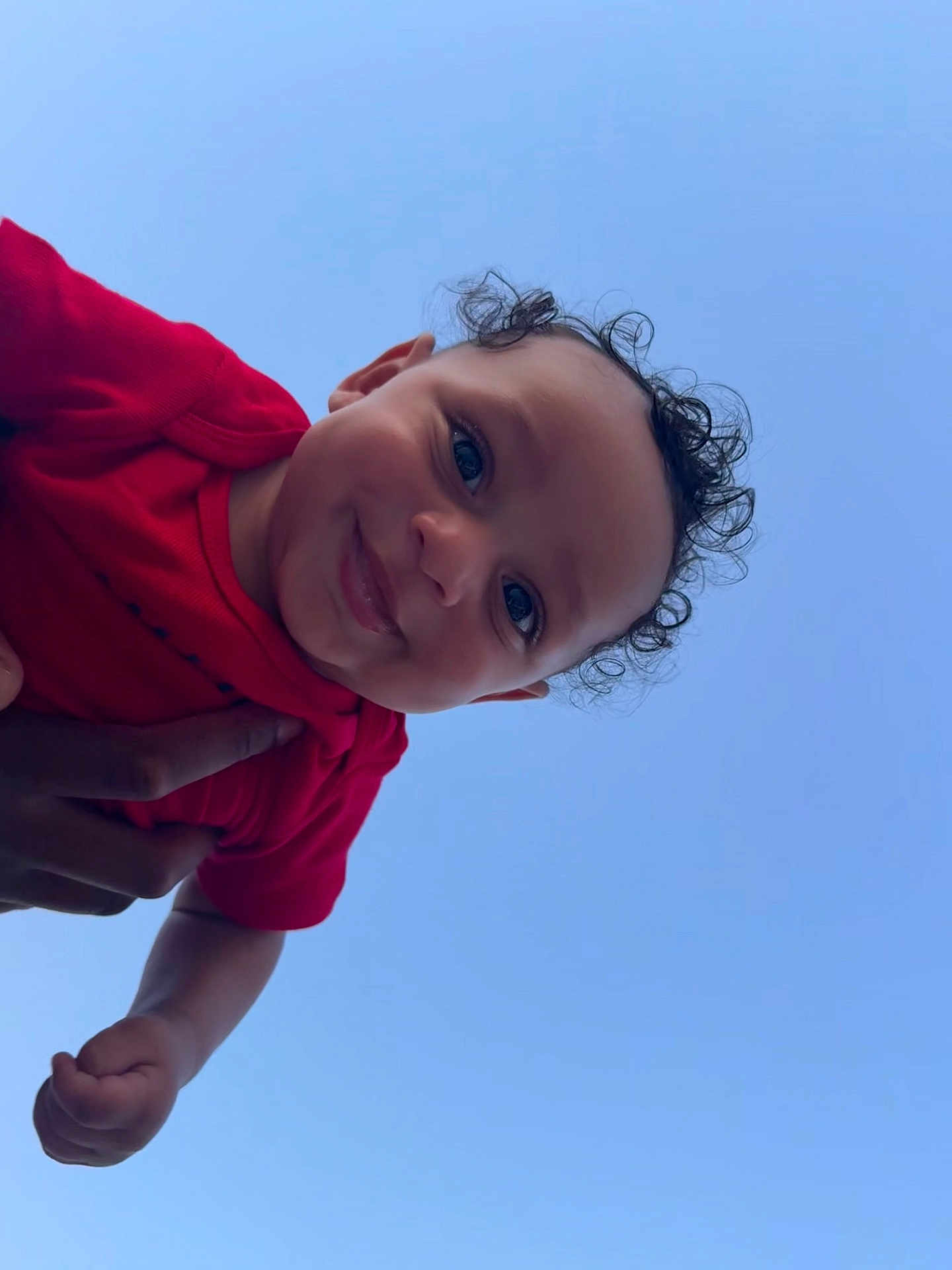 Legend joined the competition — help win amazing prizes! baby, child, curly_hair, smile, red_clothing, blue_sky, happy, face, portrait, outdoor, person, cute, joyful, infant, hand, skin, eyes, head, expression, holding