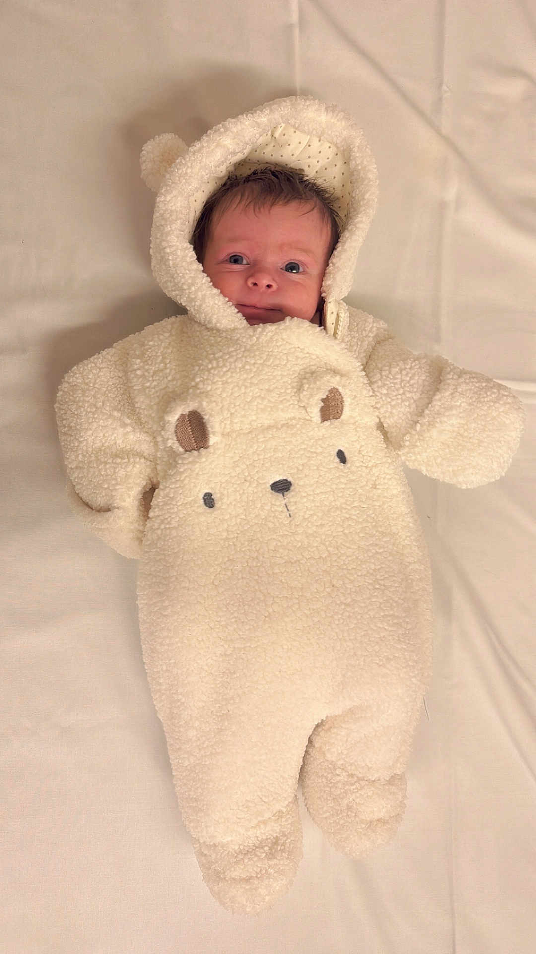 Maggie-Olwen is registered to the contest to win money with this photo: baby, infant, onesie, hood, bear_ears, cute, cozy, soft_texture, lying_down, blanket, portrait, child, smiling, face, clothing, warm, indoor, newborn, adorable, babywear