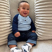 Gabriel is registered to the contest to win money with this photo: baby, child, smiling, sitting, blue_shirt, jeans, sneakers, cushions, plush, indoors, happy, cute, portrait, casual_clothing, infant, young_child, fashion, comfortable, closeup, cozy