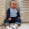 baby, child, smiling, sitting, blue_shirt, jeans, sneakers, cushions, plush, indoors, happy, cute, portrait, casual_clothing, infant, young_child, fashion, comfortable, closeup, cozy