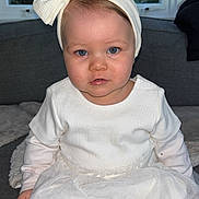Lexy a rejoint le concours — aidez-le/la à gagner de superbes lots ! baby, child, girl, white_dress, headband, bow, sitting, indoor, couch, window, curtains, blue_eyes, portrait, cute, infant, clothing, face, person, toddler, home