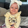 Lexy a rejoint le concours — aidez-le/la à gagner de superbes lots ! baby, child, smiling, headband, bow, yellow_top, floral_pants, sitting, couch, indoor, window, blanket, person, cute, portrait, happy, blue_eyes, infant, home, cozy