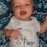 Steven joined the competition — help win amazing prizes! baby, infant, onesie, smiling, face, eyes, mouth, hand, fingers, blanket, patterned_blanket, teal, blue, portrait, cute, chubby_cheeks, lying_down, close_up, indoors, happy