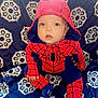 Steven is registered to the contest to win money with this photo: baby, infant, child, spiderman_costume, hood, red, blue, blanket, patterned_background, sitting, cute, wide_eyed, portrait, onesie, fabric, hand, foot, indoor, playful, costume