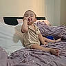 Miguel joined the competition — help win amazing prizes! toddler, child, bed, pajamas, teddy_bear, purple_bedspread, pillow, indoors, sitting, smiling, thumb_sucking, cozy, blanket, person, cute, relaxed, home, furniture, sleepwear, young_child