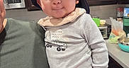 Miguel is registered to the contest to win money with this photo: baby, child, hat, onesie, person, indoor, kitchen, cabinet, adult, holding, face, expression, cute, clothing, hand, toy, countertop, appliance, smile, portrait